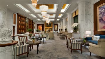 A spacious lobby with marble columns, chandeliers, and a variety of seating arrangements including sofas and armchairs.