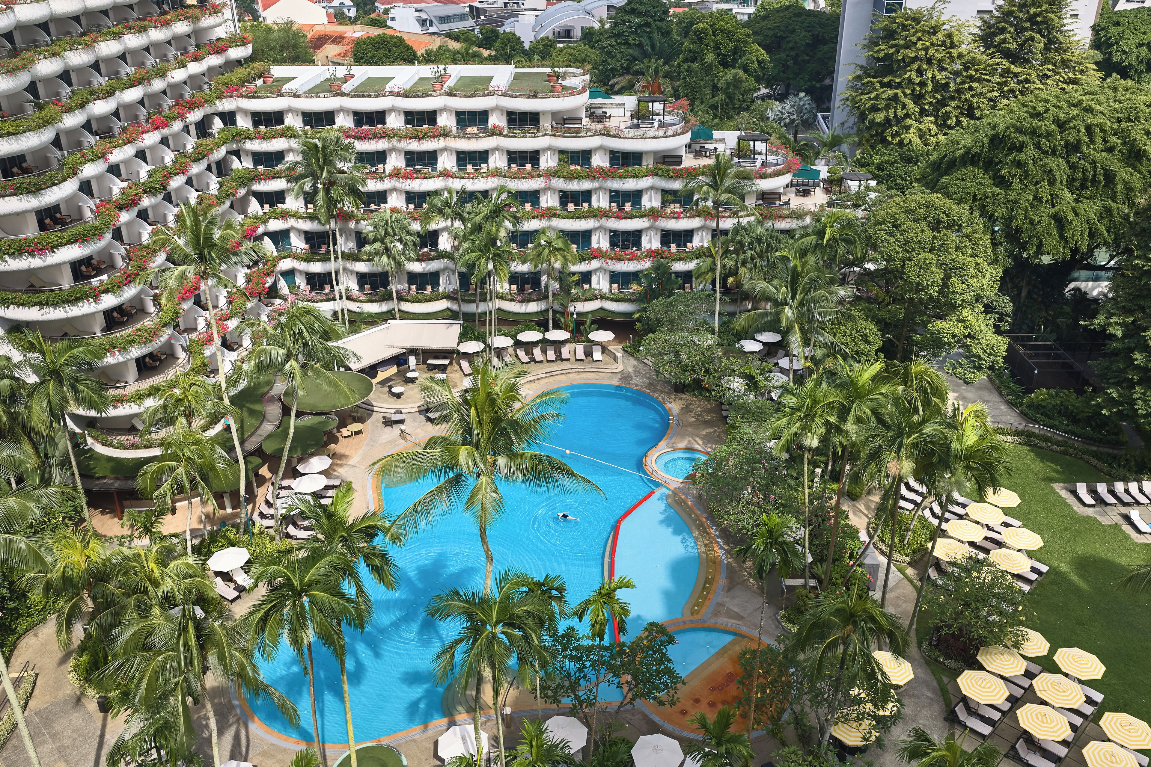 Un hotel de varios pisos con una piscina central rodeada de palmeras y tumbonas.