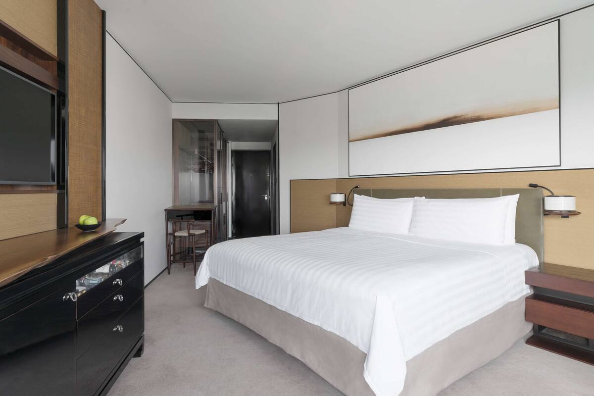 Une chambre d’hôtel avec un grand lit, une commode en bois, un bureau et un téléviseur fixé au mur.