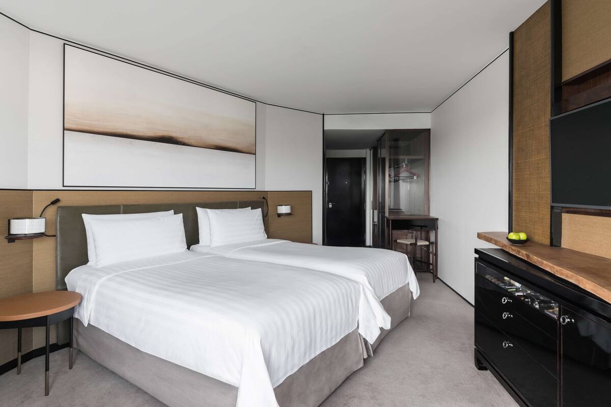 Une chambre d’hôtel moderne avec un grand lit, une petite table, une commode et un grand tableau abstrait accroché au mur.