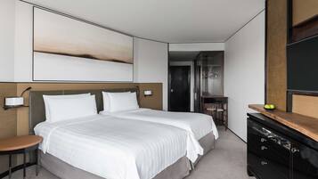 A modern hotel room with a large bed, a small table, a dresser, and a large abstract painting on the wall.