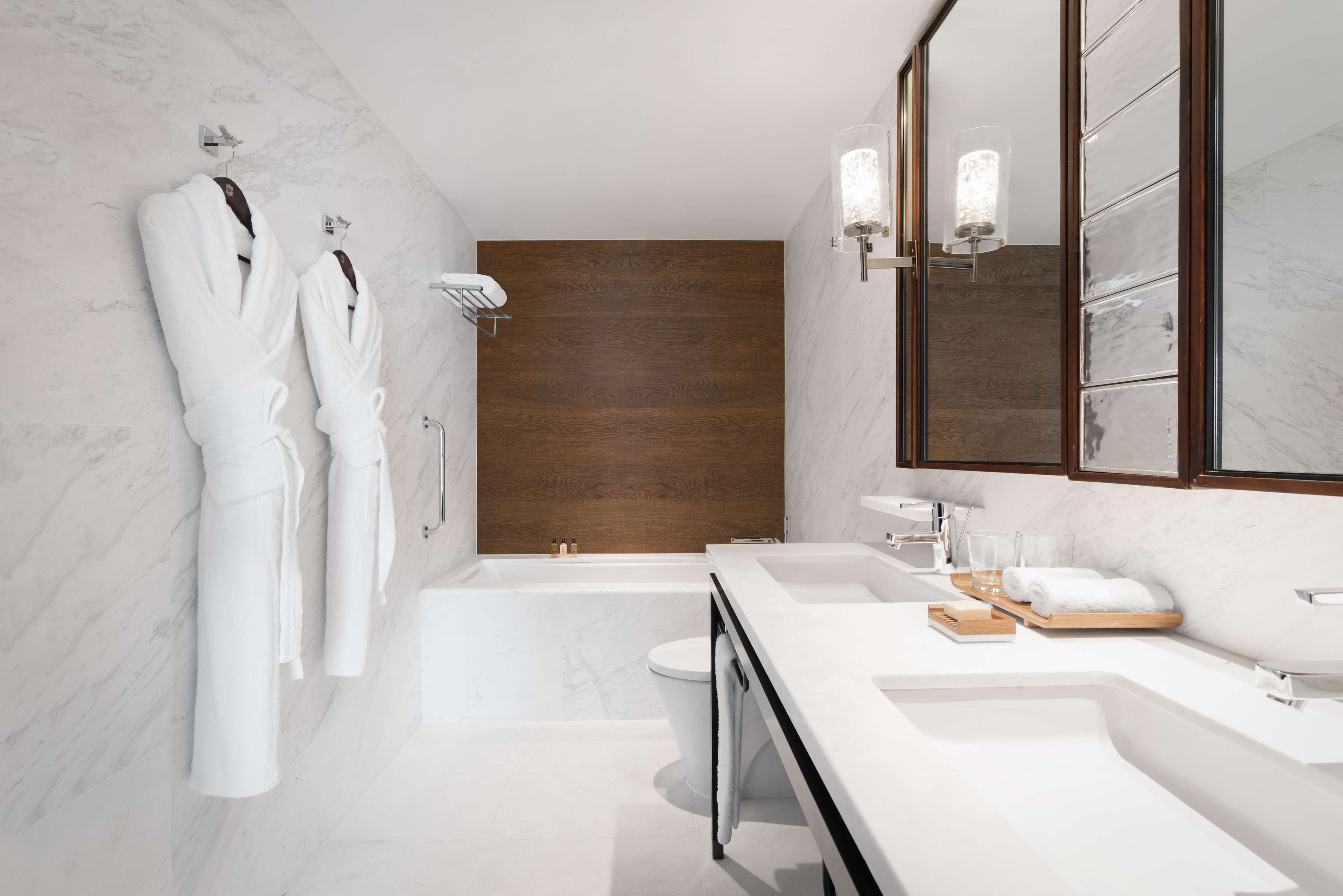 A modern bathroom with a marble floor, a wooden accent wall, a large mirror, and a bathtub.