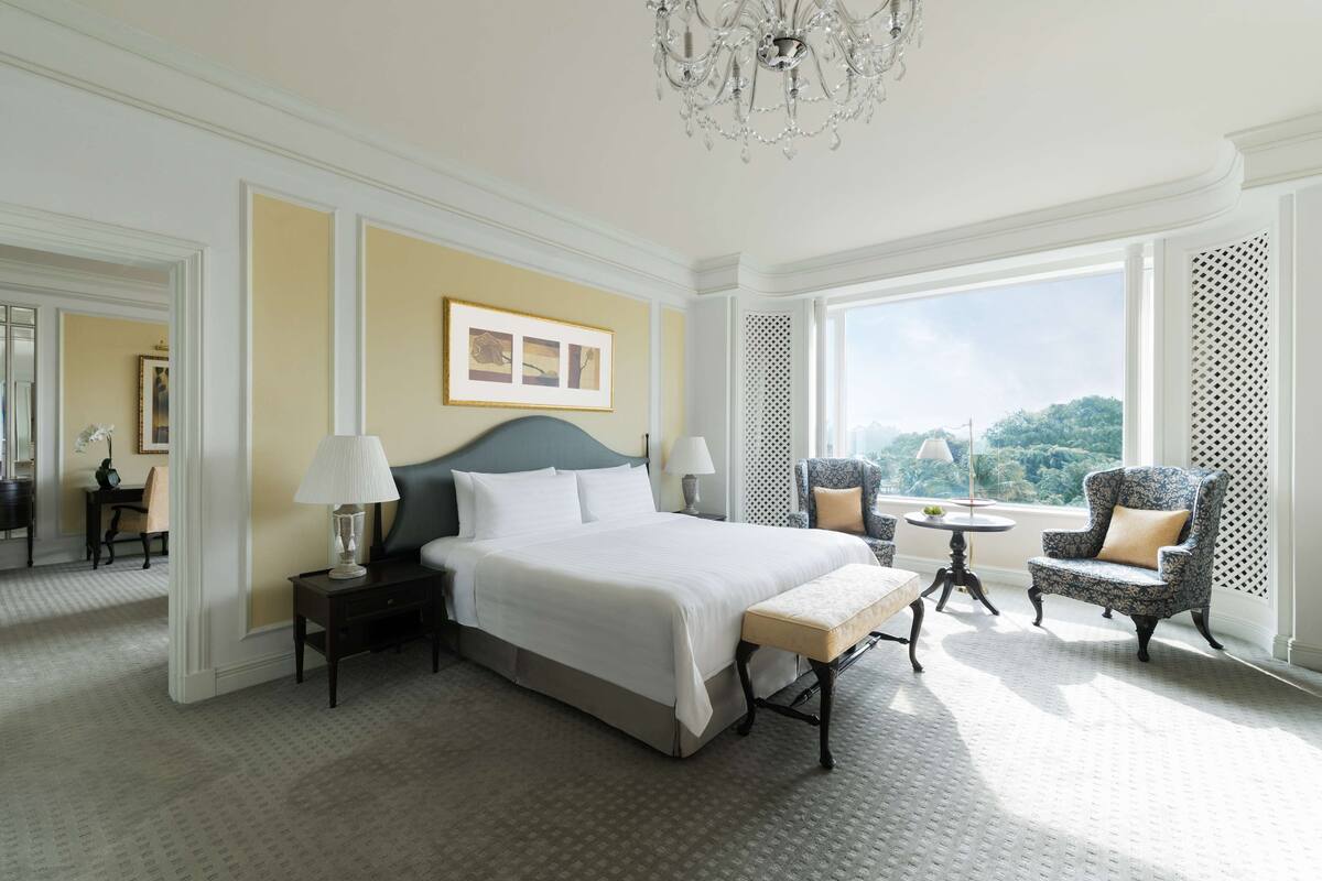 Une chambre spacieuse avec un grand lit, un coin salon avec un fauteuil et une table, et une vue sur l’extérieur.