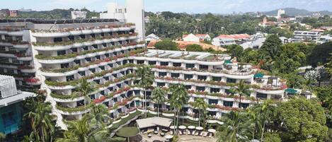 A multi-story hotel with balconies, a swimming pool, and lush greenery.