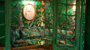 A room with a green patterned wall, a sofa, a round table, and a mirror.