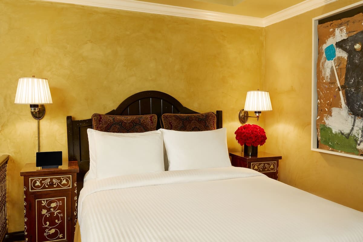 A hotel room with a large bed, two bedside tables with lamps, a decorative headboard, and a painting on the wall.