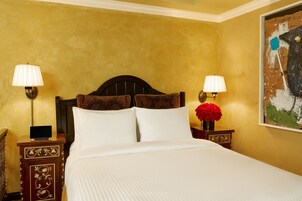 Una habitación de hotel con una cama grande, dos mesitas de noche con lámparas, un cabecero decorativo y un cuadro en la pared.