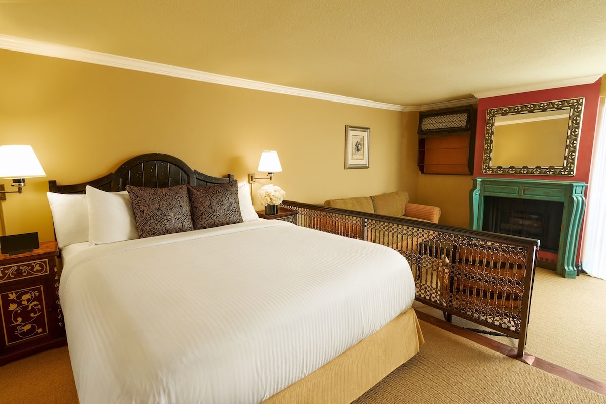 A hotel room with a large bed, two bedside lamps, a fireplace, and a mirror on the wall.