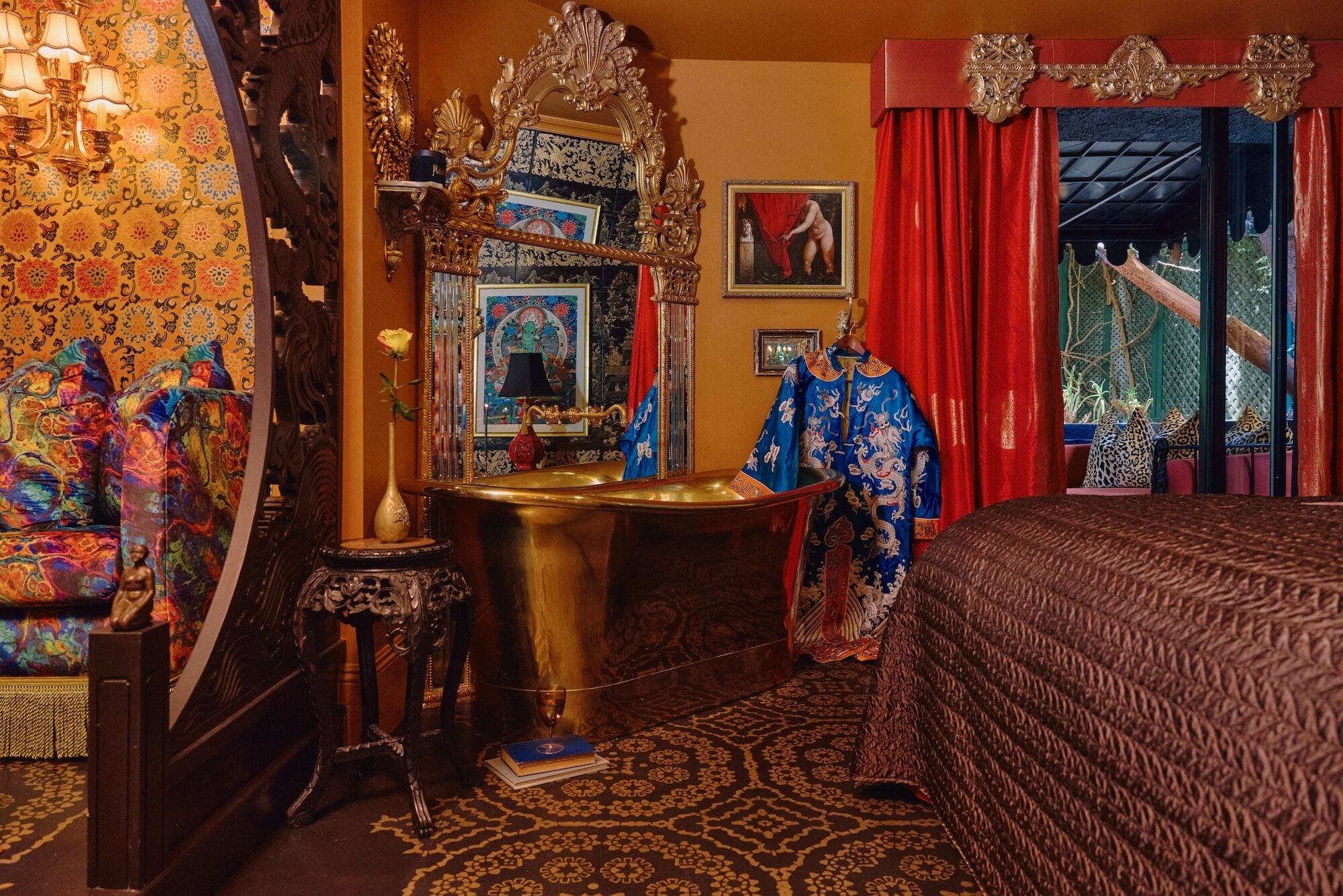 A room with a bed, a vanity with a mirror, a chandelier, and a red curtain.