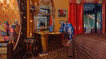 A room with a bed, a vanity with a mirror, a chandelier, and a red curtain.