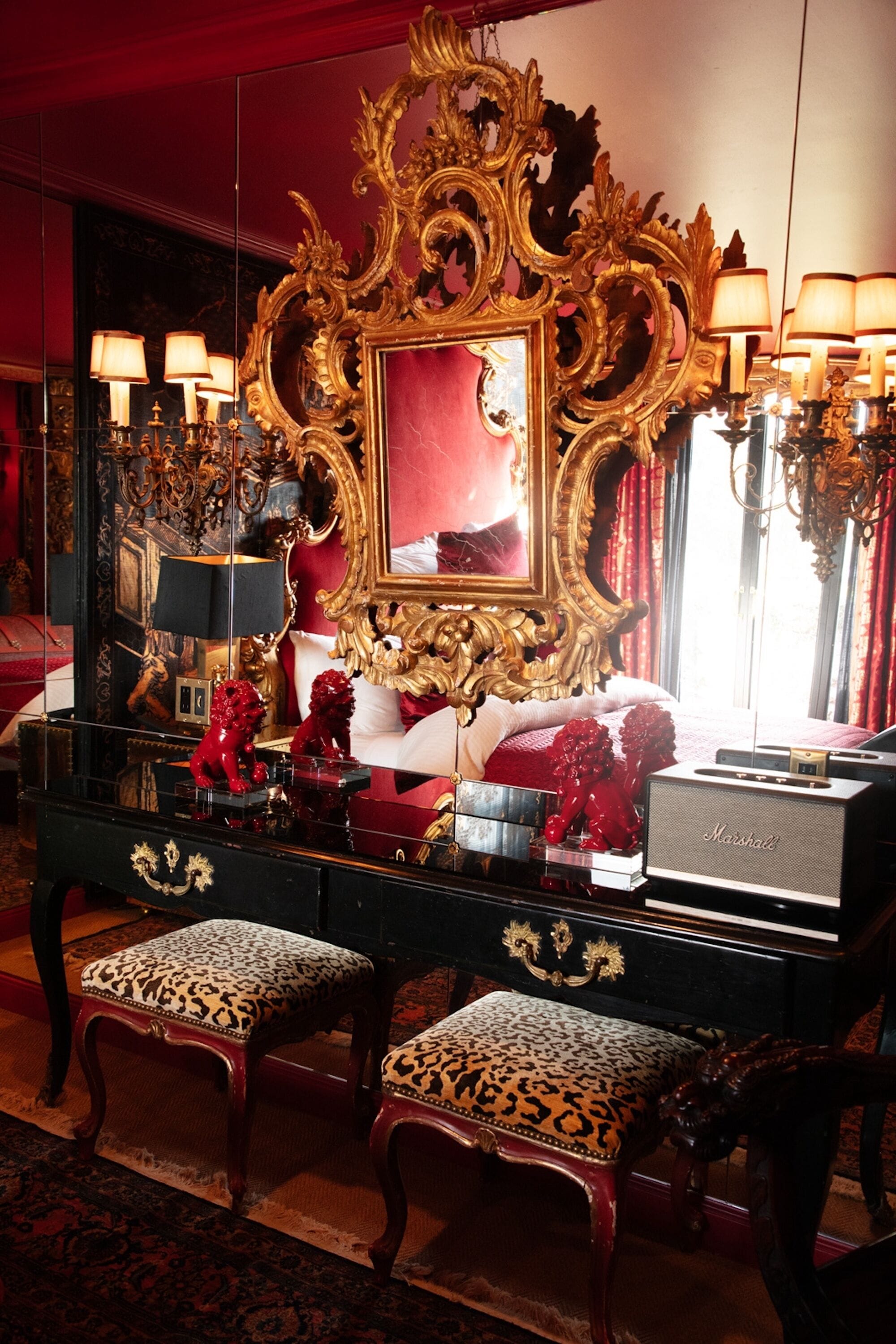 Ein luxuriöser Raum mit einem großen, verzierten Spiegel, einem schwarzen Schminktisch mit zwei Hocker mit Leopardenmuster und einem rot gepolsterten Bett.