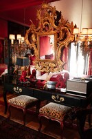 A luxurious room with a large ornate mirror, a black vanity with two leopard-print stools, and a red upholstered bed.