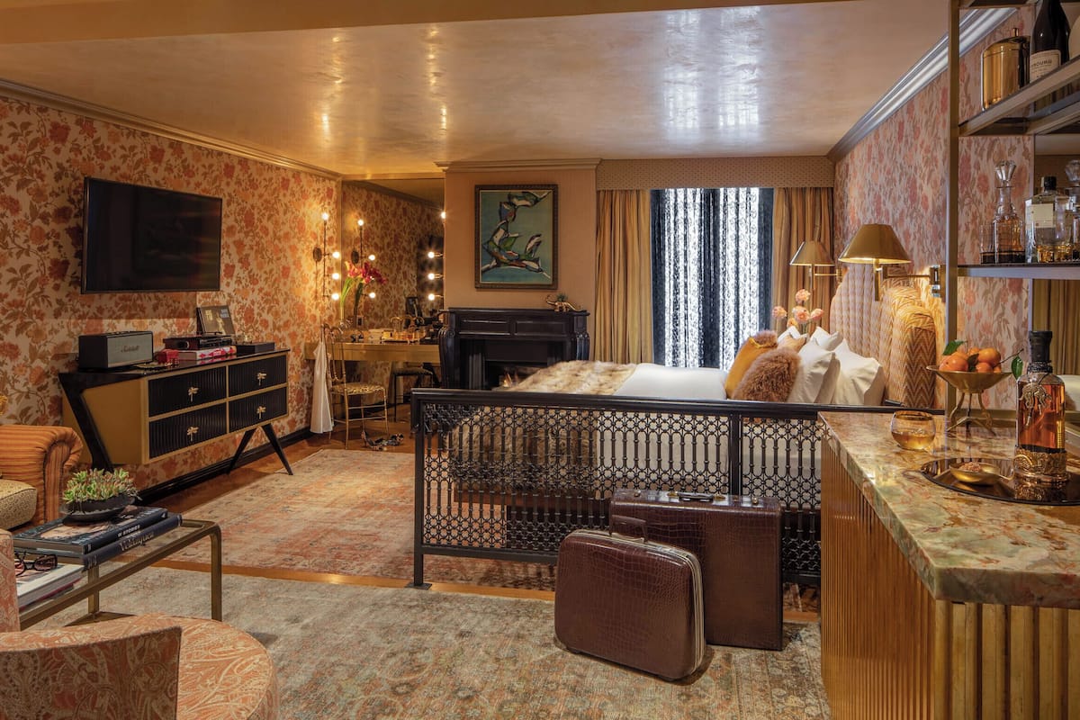 A hotel room with a bed, a desk, a television, a fireplace, and a bar area.