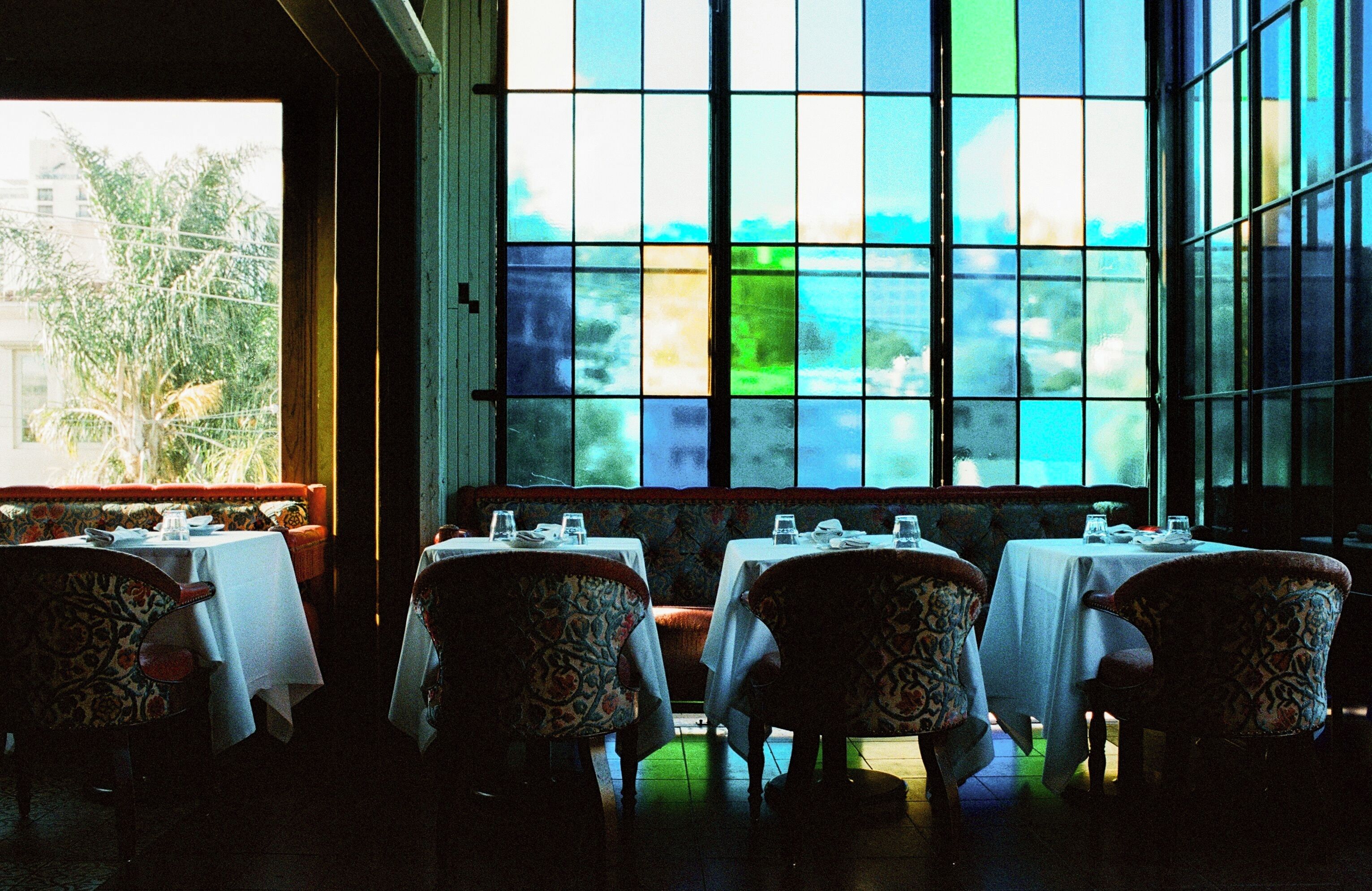 A restaurant with tables and chairs, large windows, and a view of trees and buildings.