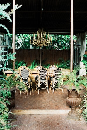 An outdoor dining area with a table and chairs, surrounded by plants and a wooden fence. - Petit Ermitage (West Hollywood)
