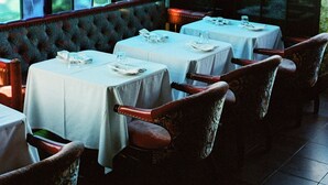 A restaurant with multiple tables, a cushioned bench, and large windows. - Petit Ermitage (West Hollywood)