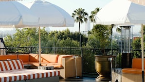 A poolside area with a white canopy, orange and white striped lounge chairs, and a clear view of palm trees. - Petit Ermitage (West Hollywood)