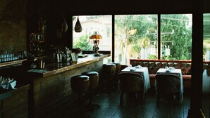A restaurant with a bar area, tables, and a view of greenery outside. - Petit Ermitage (West Hollywood)