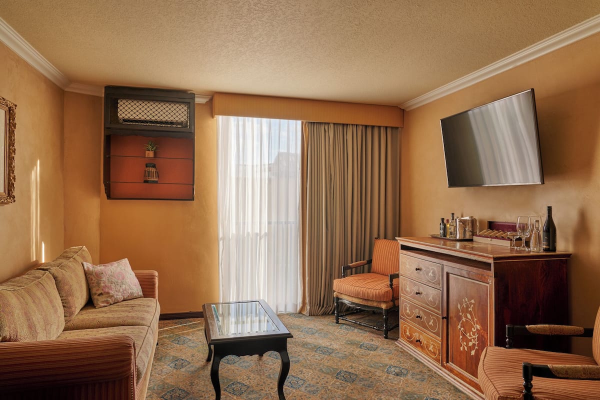 A hotel room with a sofa, armchair, a small table, a cabinet, and a TV mounted on the wall.