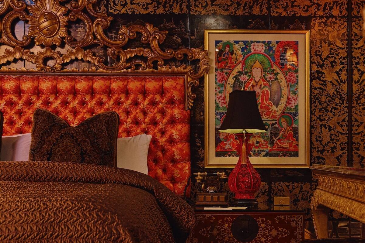 A traditional room with a tufted headboard, a red lamp, and a framed painting.