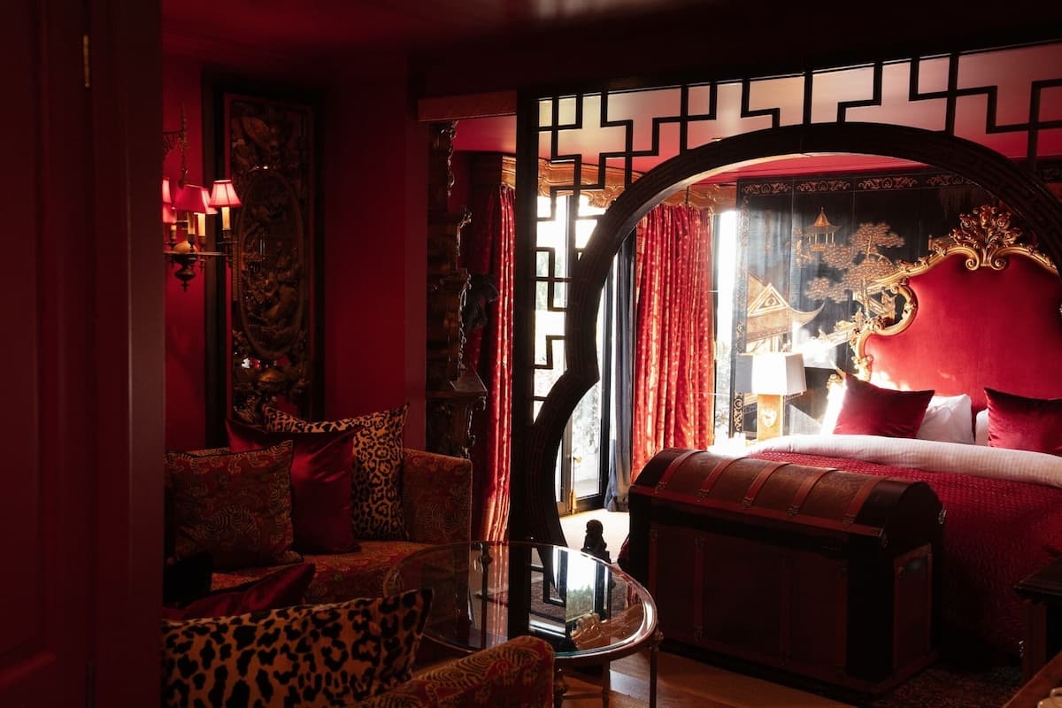 A room with a bed, a glass table, a leopard print chair, and a red curtain.