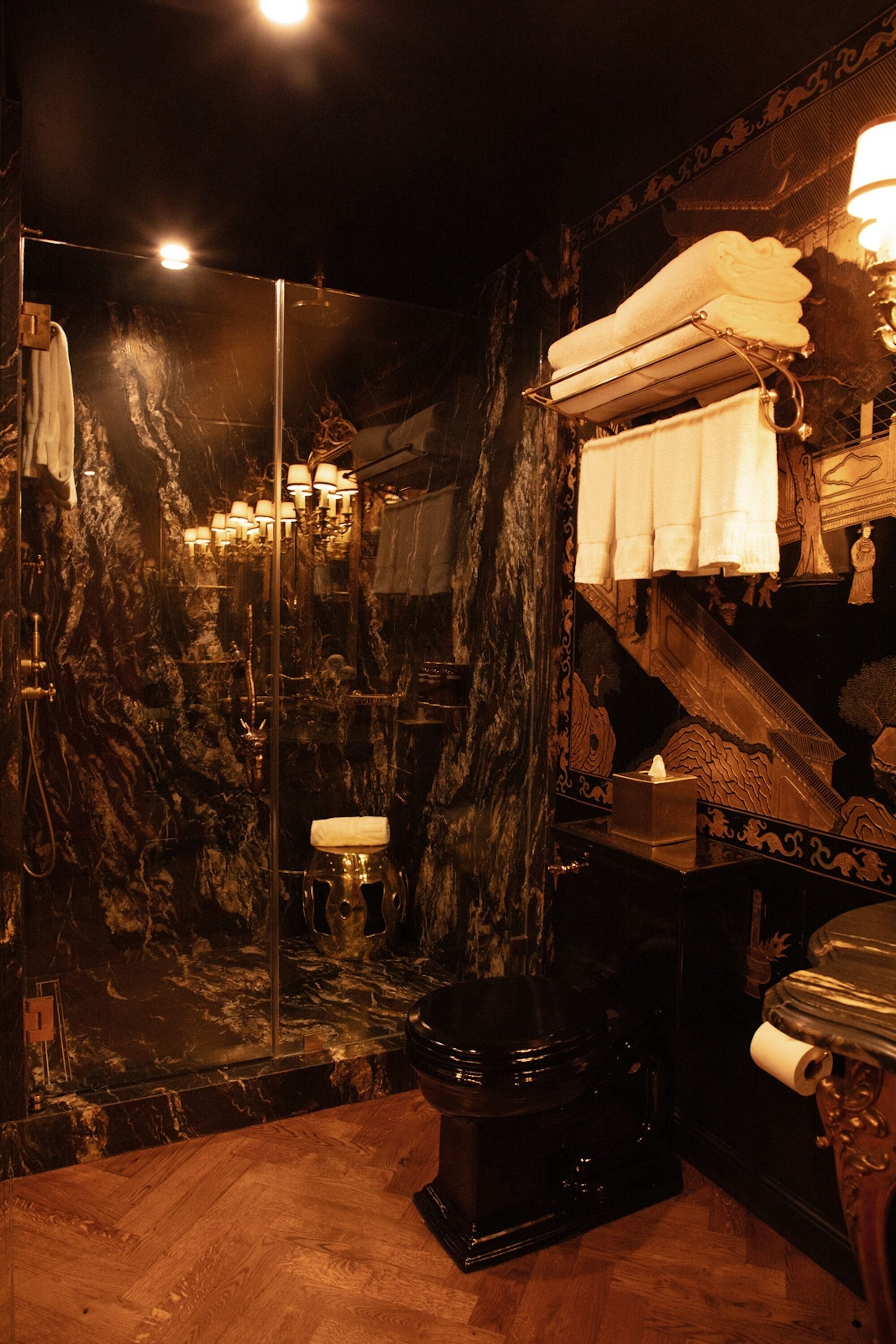 A bathroom with a marble wall, a shower, a toilet, and a sink.