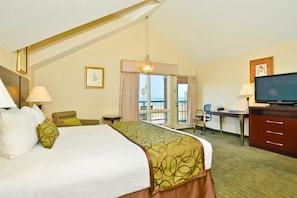 A hotel room with a large bed, a desk with a computer, a television, and a balcony with a view.