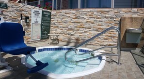 A small outdoor hot tub with a stone wall backdrop, a blue chair, and a sign indicating spa rules and emergency shut-off valve switch. - Best Western Plus Dana Point Inn-by-the-sea (Dana Point)