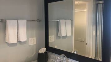 A bathroom with a large mirror, a sink, and two towels hanging on a towel bar.