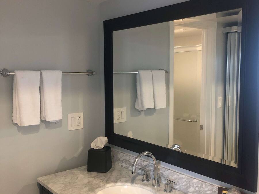 A bathroom with a large mirror, a sink, and two towels hanging on a towel bar.
