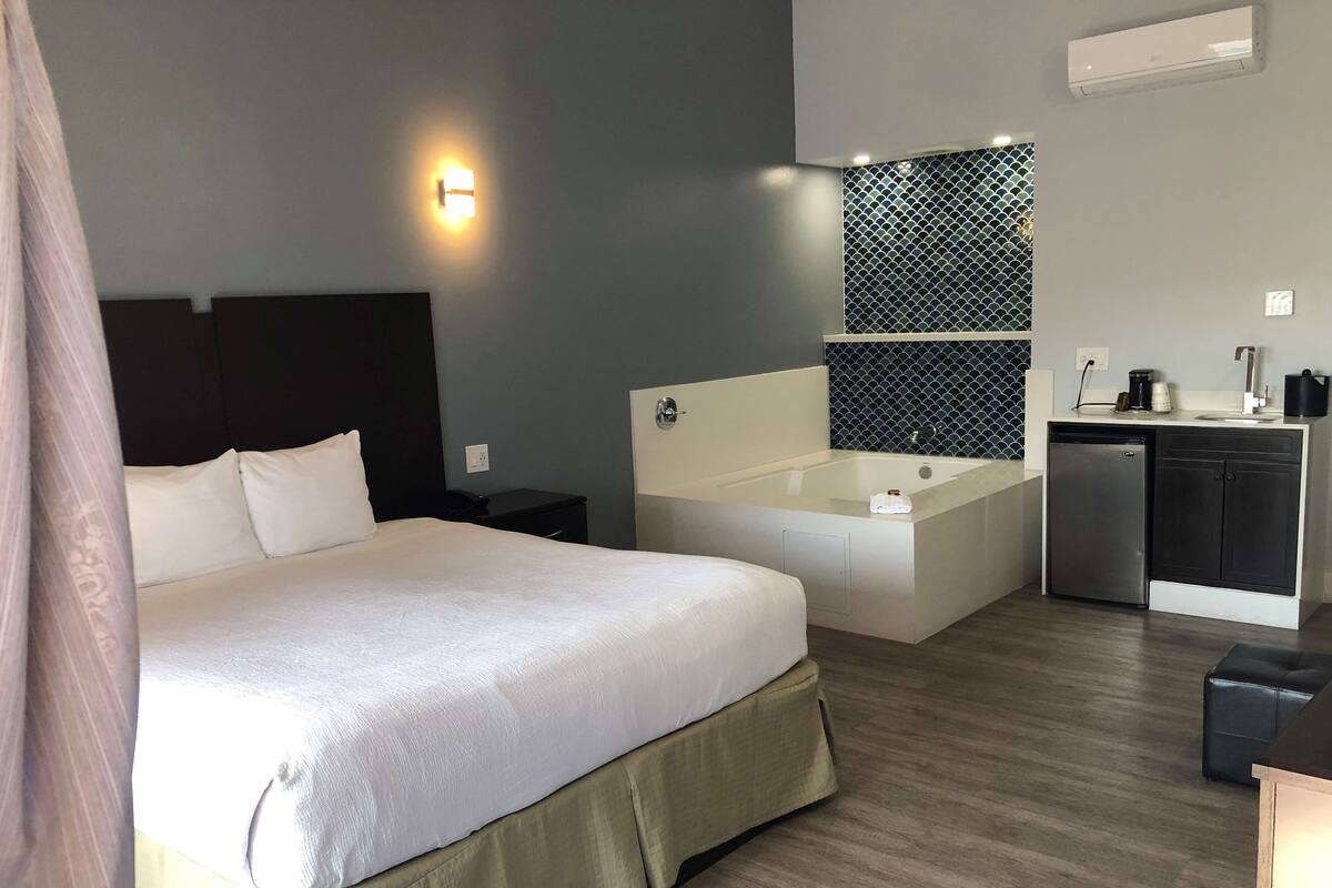 Ett hotellrum med en stor säng, ett litet skrivbord, ett inbyggt badkar och ett litet pentry.