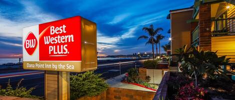 A hotel sign reading "Best Western PLUS" with a view of the sea and a cityscape in the background.