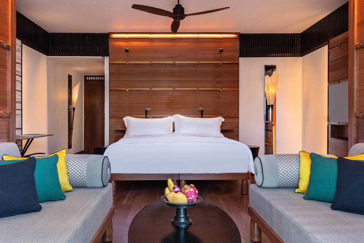Ein modernes Hotelzimmer mit einem großen Bett, zwei Sofas, einem Deckenventilator und einem Nachttisch mit Lampe.