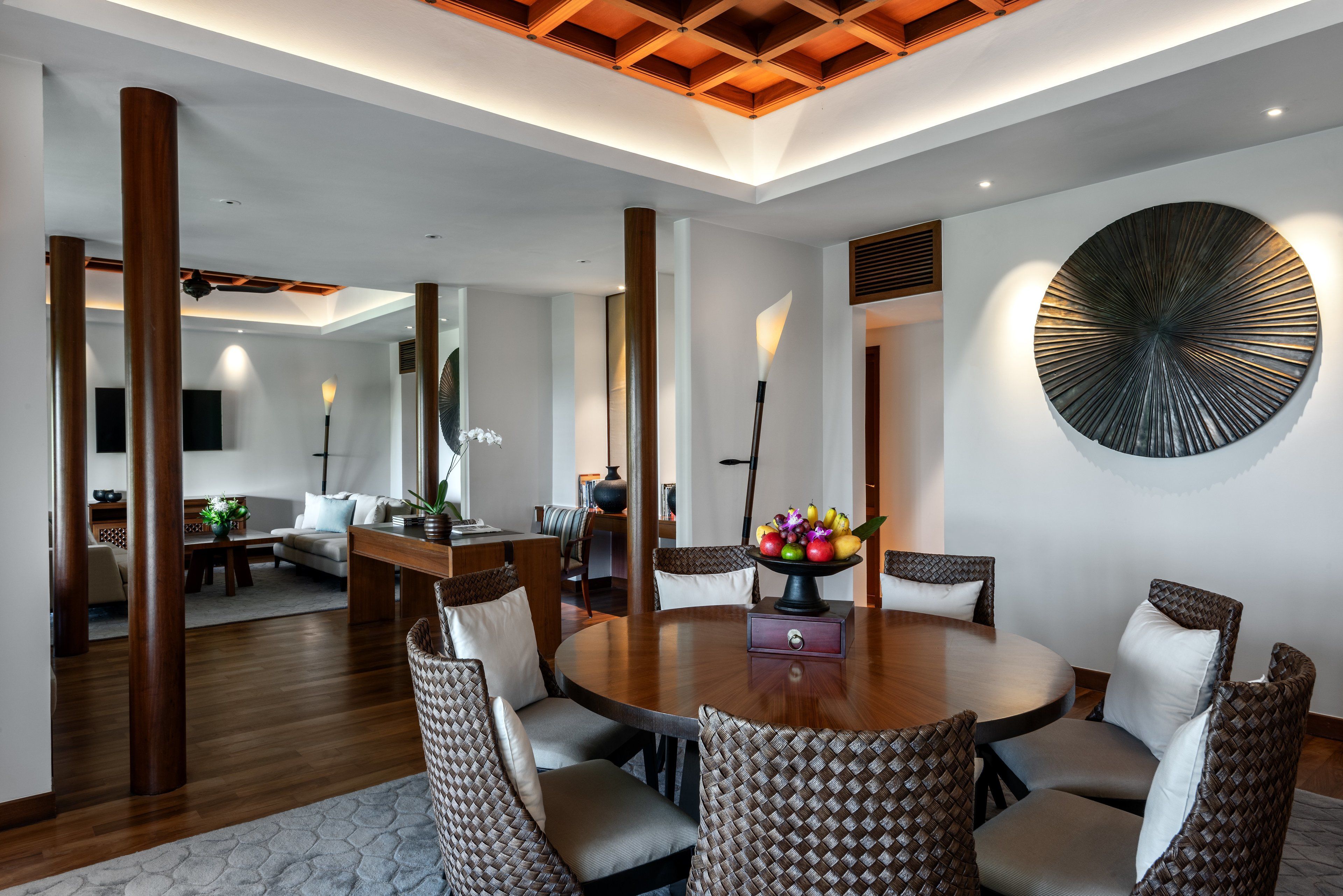 A modern dining area with a round table, cushioned chairs, and a decorative wall piece.