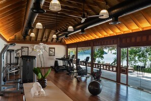 A gym with exercise equipment, a large window with a view of the water, and a wooden ceiling.