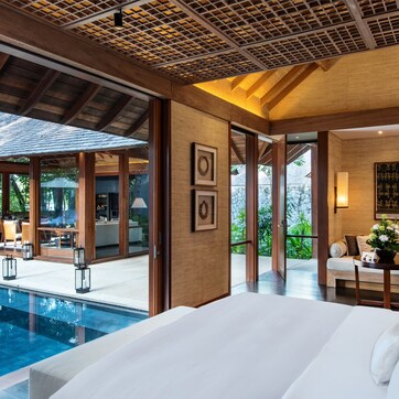 A modern hotel room with a large bed, a pool, and a dining area with outdoor seating.