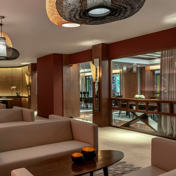 A modern hotel lobby with multiple seating areas, a wooden reception desk, and large windows offering views of the interior.