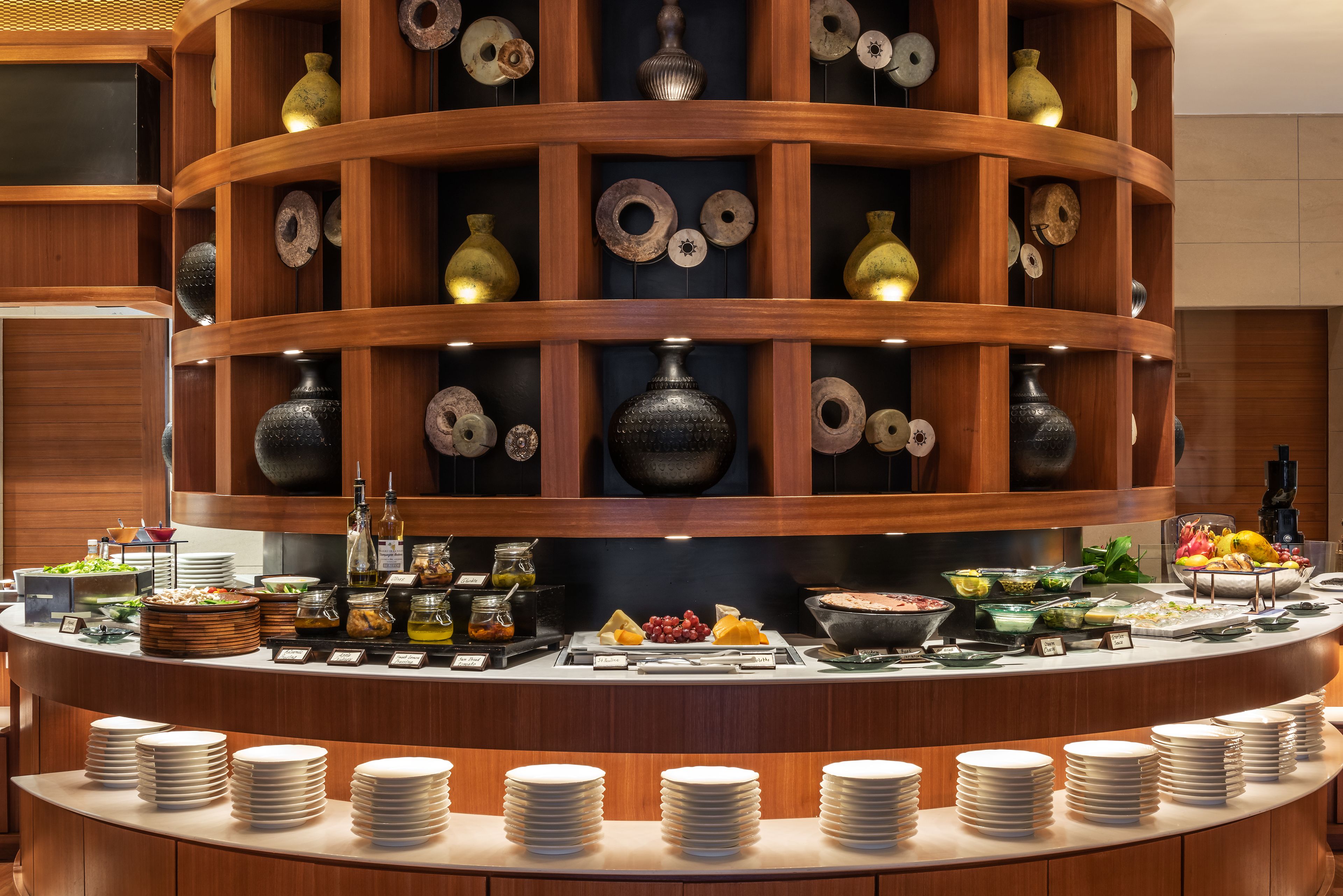 A buffet setup with multiple serving stations, a variety of food items, and a decorative wooden structure with vases.