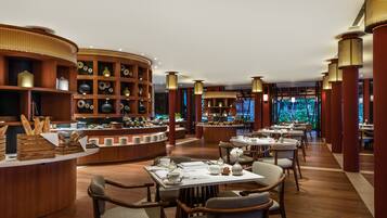 A modern restaurant with wooden furniture, a buffet area, and a view of greenery through large windows.