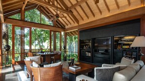 Una habitación amplia con techo de madera, ventanas grandes, chimenea y una zona de estar con sofá y sillones.