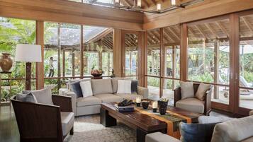 A spacious indoor area with a wooden ceiling, large windows, and a seating arrangement including sofas and a coffee table.
