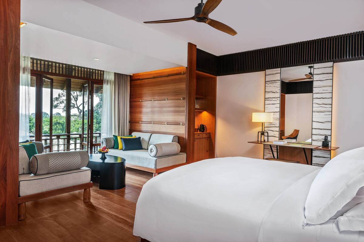 Ein modernes Hotelzimmer mit einem großen Bett, einer Sitzecke, einem Schreibtisch und Blick ins Freie.