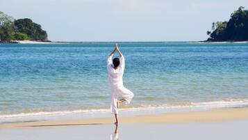Une personne effectuant une posture de yoga sur une plage, avec une eau bleue et limpide et une terre ferme visible au loin.