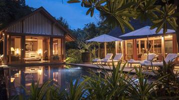 A resort with a swimming pool, lounge chairs, and a well-lit bedroom area.