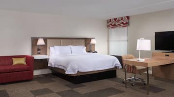 Una habitación de hotel con una cama, un escritorio, un televisor, un sofá rojo y una silla.