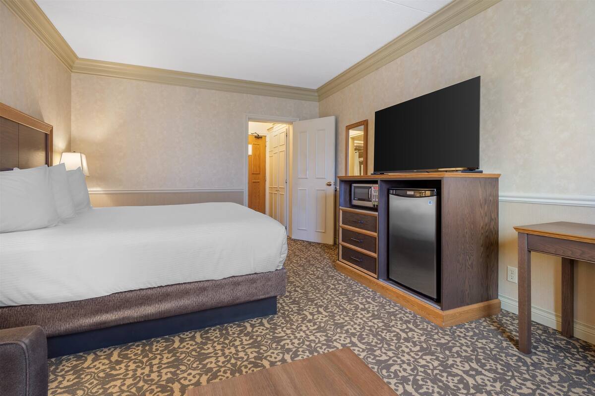 A hotel room with a bed, a flat-screen TV, a microwave, and a wooden side table.