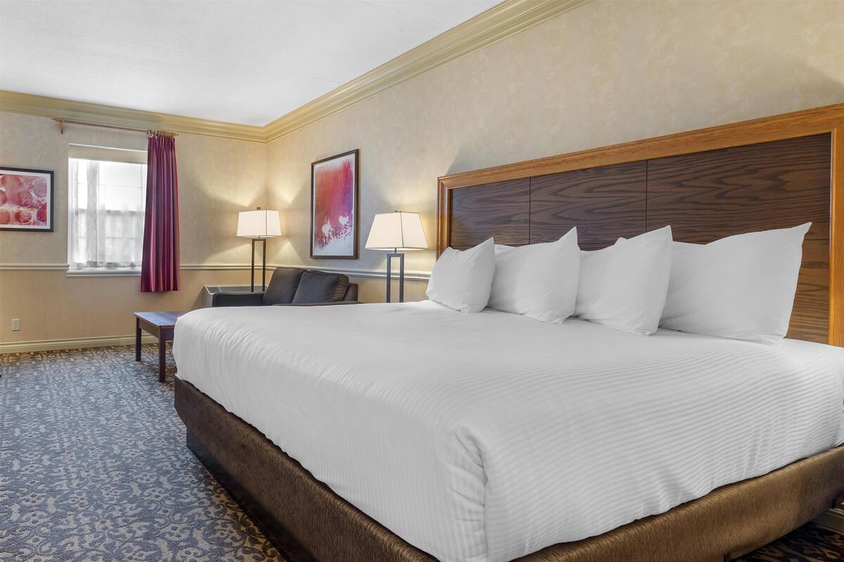 A hotel room with a large bed, a desk, a chair, a lamp, and a window with curtains.