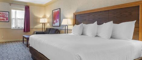 A hotel room with a large bed, a desk, a chair, a lamp, and a window with curtains.
