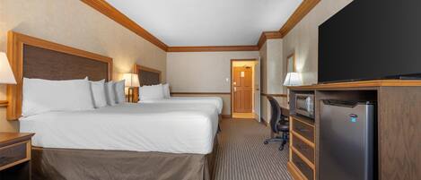 A hotel room with two beds, a television, a refrigerator, and a desk with a lamp.