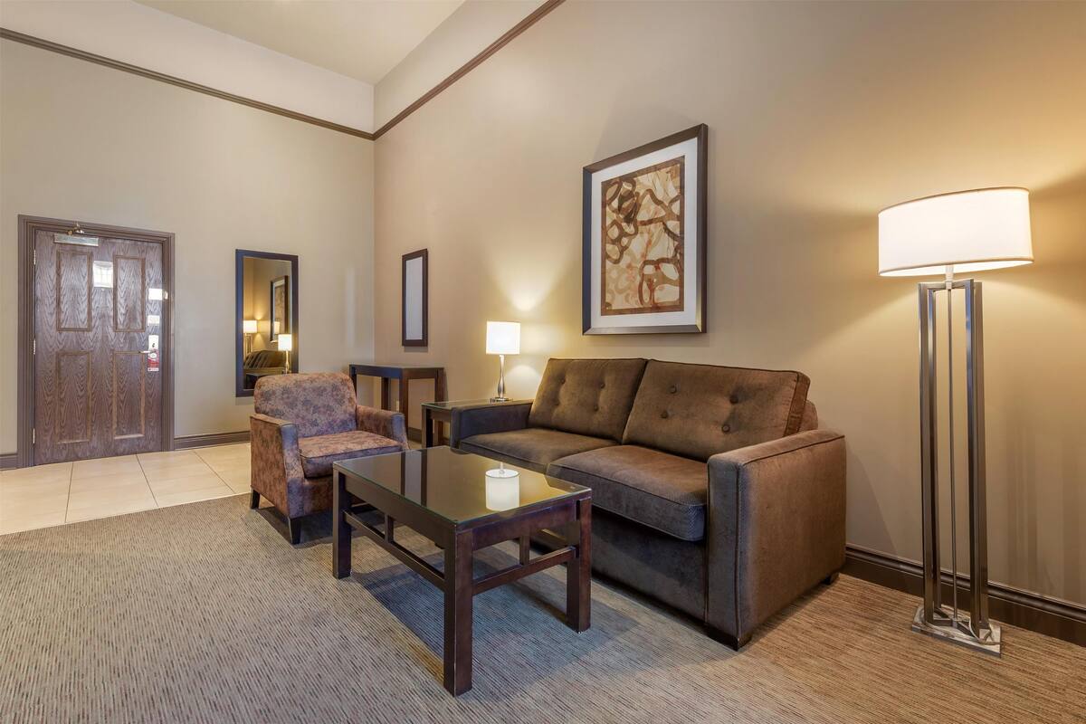 A modern living room with a brown sofa, a patterned armchair, a glass coffee table, and a floor lamp.